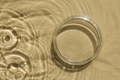 Photo of Stylish presentation for product. Glass podium in water on sand, top view. Space for text