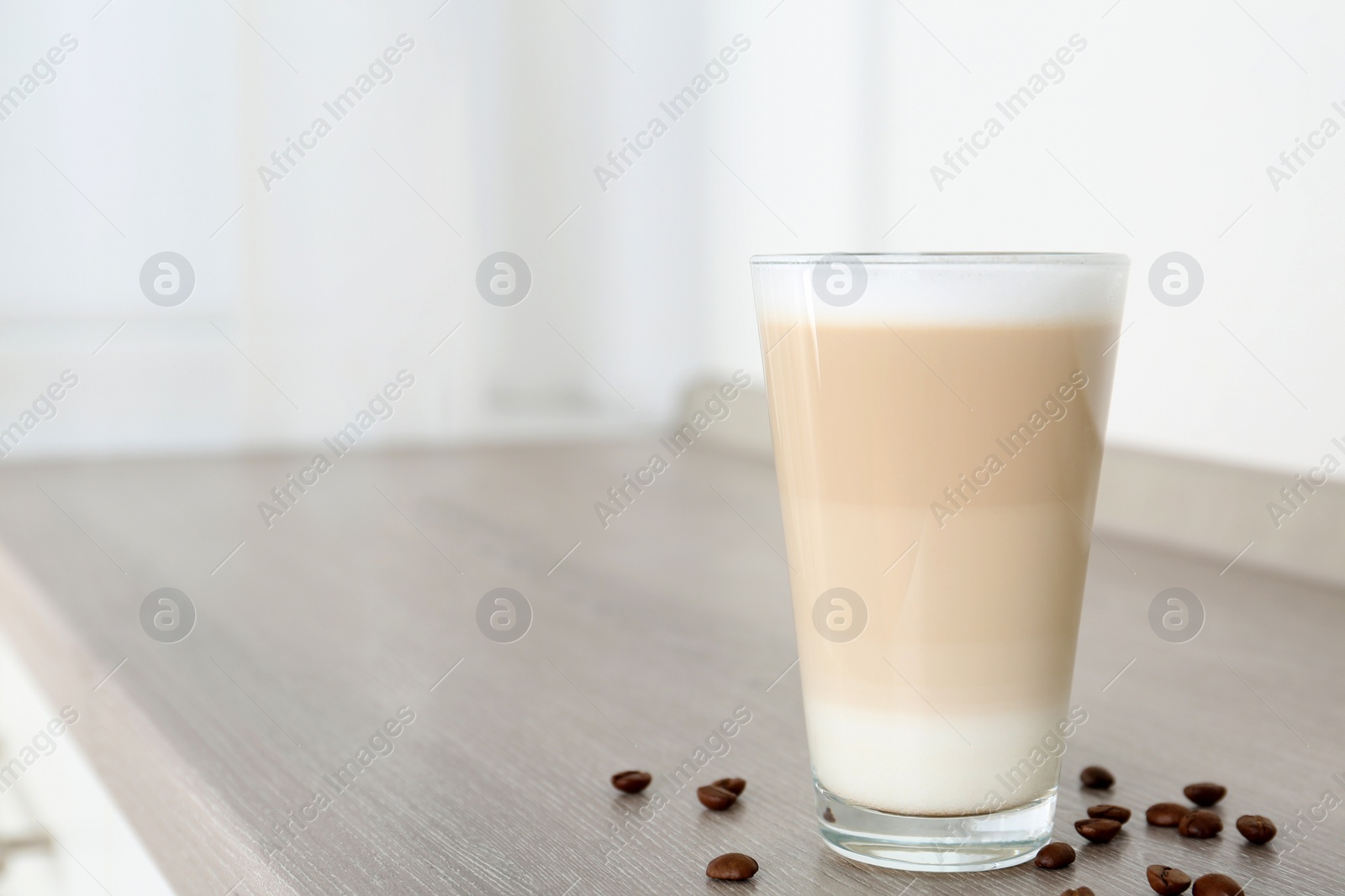 Photo of Delicious latte macchiato and coffee beans on wooden table indoors. Space for text