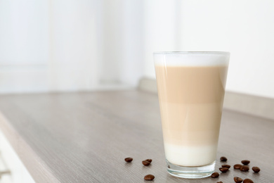 Photo of Delicious latte macchiato and coffee beans on wooden table indoors. Space for text