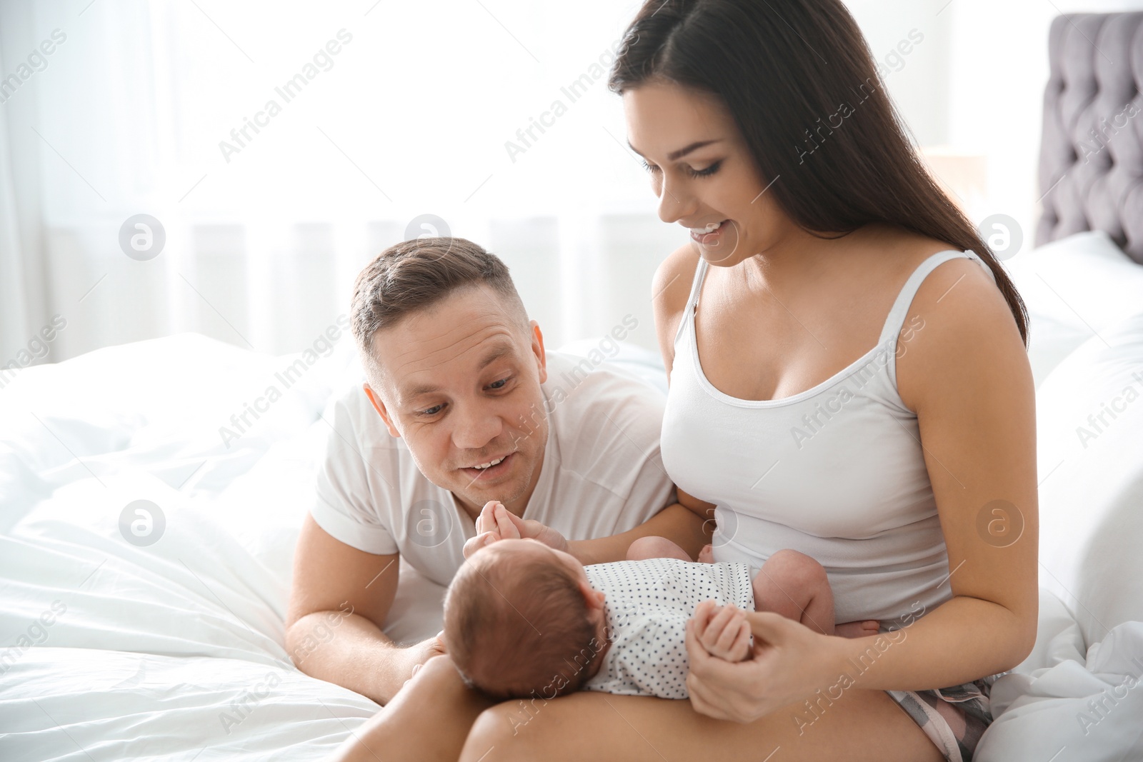 Photo of Happy couple with their newborn baby on bed