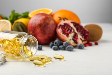 Photo of Vitamin pills, bottle and fresh fruits on white wooden table. Space for text