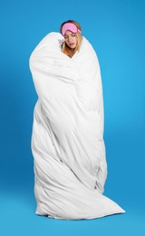 Photo of Young woman in sleeping mask wrapped with soft blanket on blue background