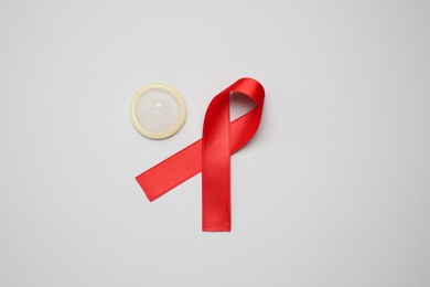 Photo of Red ribbon and condom on light grey background, flat lay. AIDS disease awareness