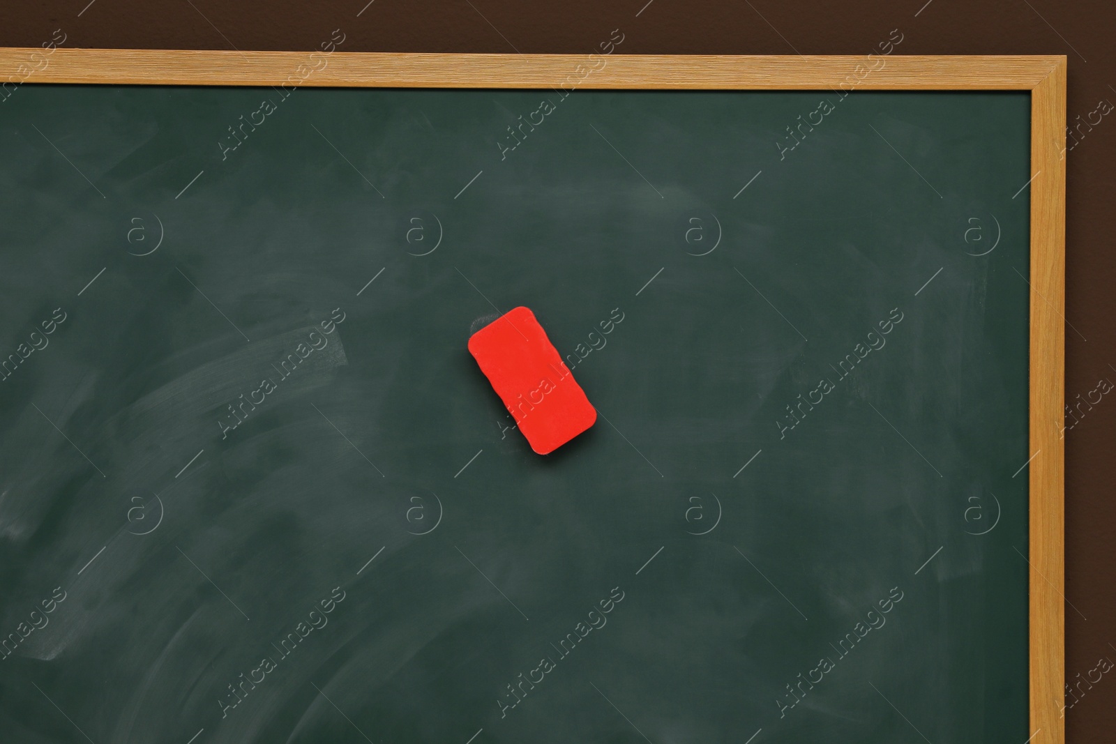 Photo of Dirty green chalkboard with duster hanging on brown wall