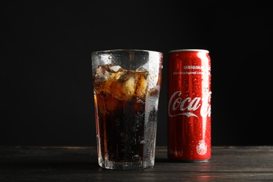 Photo of MYKOLAIV, UKRAINE - NOVEMBER 15, 2018: Glass and can with Coca Cola on table against black background