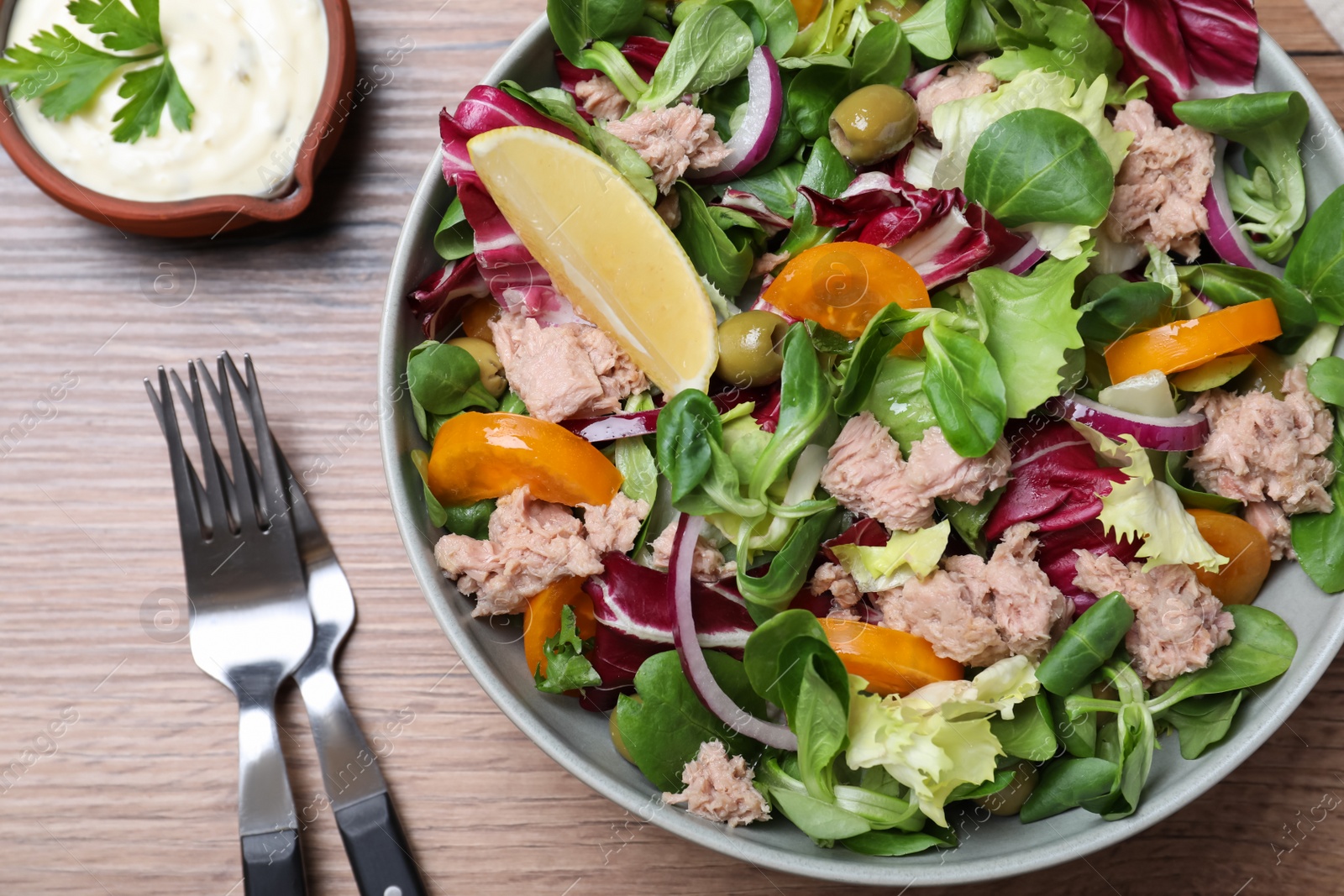 Photo of Bowl of delicious salad with canned tuna and vegetables served on wooden table, flat lay