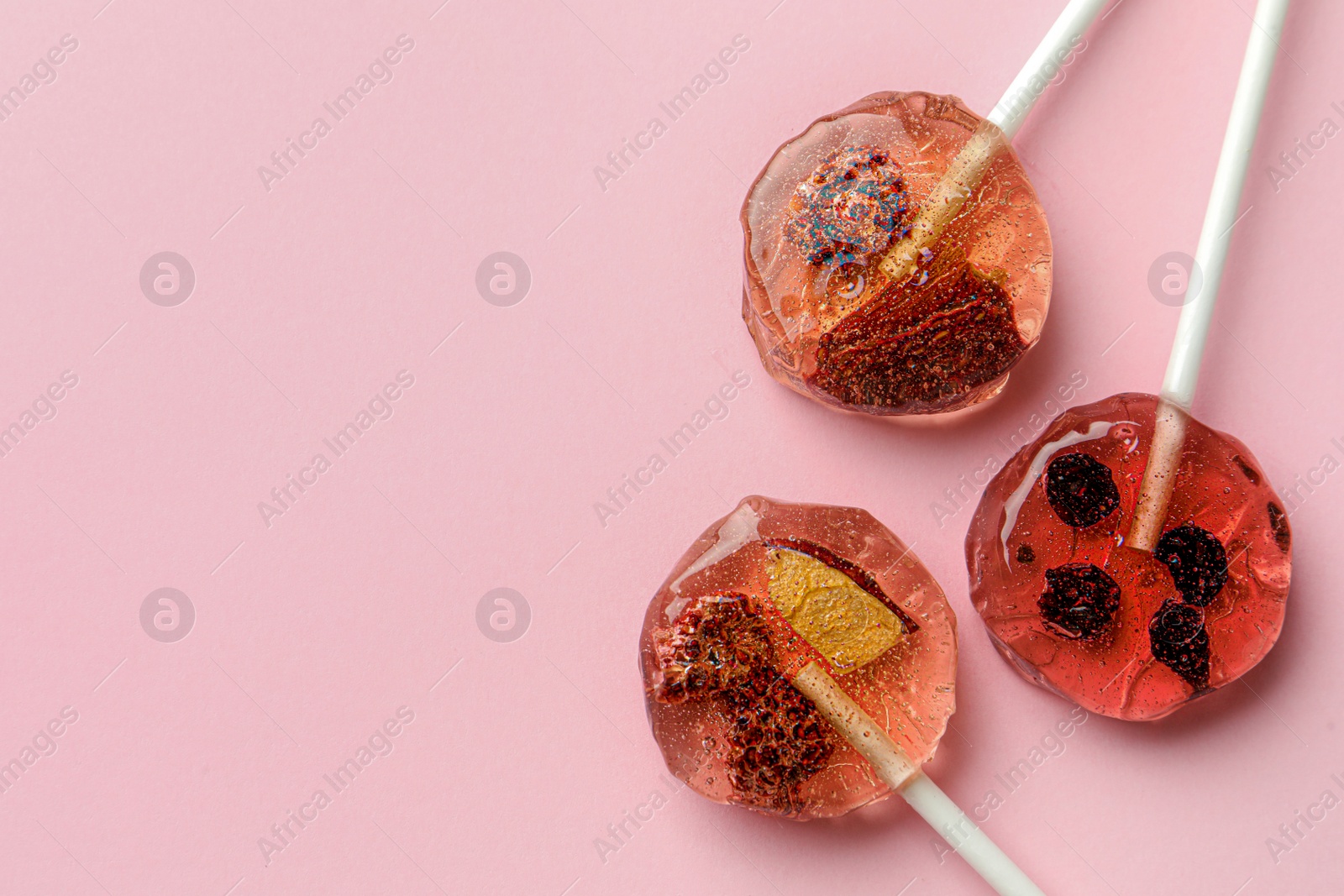 Photo of Sweet colorful lollipops with berries on pink background, flat lay. Space for text