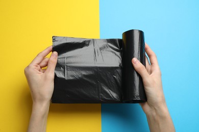 Photo of Woman holding roll of black garbage bags over color background, top view