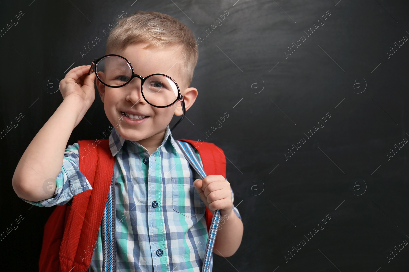 Photo of Funny little child wearing glasses near chalkboard, space for text. First time at school