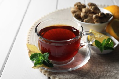 Cup of delicious ginger tea and ingredients on white wooden table, closeup