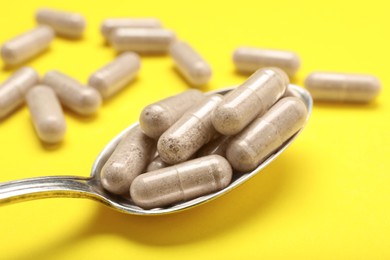 Photo of Gelatin capsules in spoon on yellow background, closeup