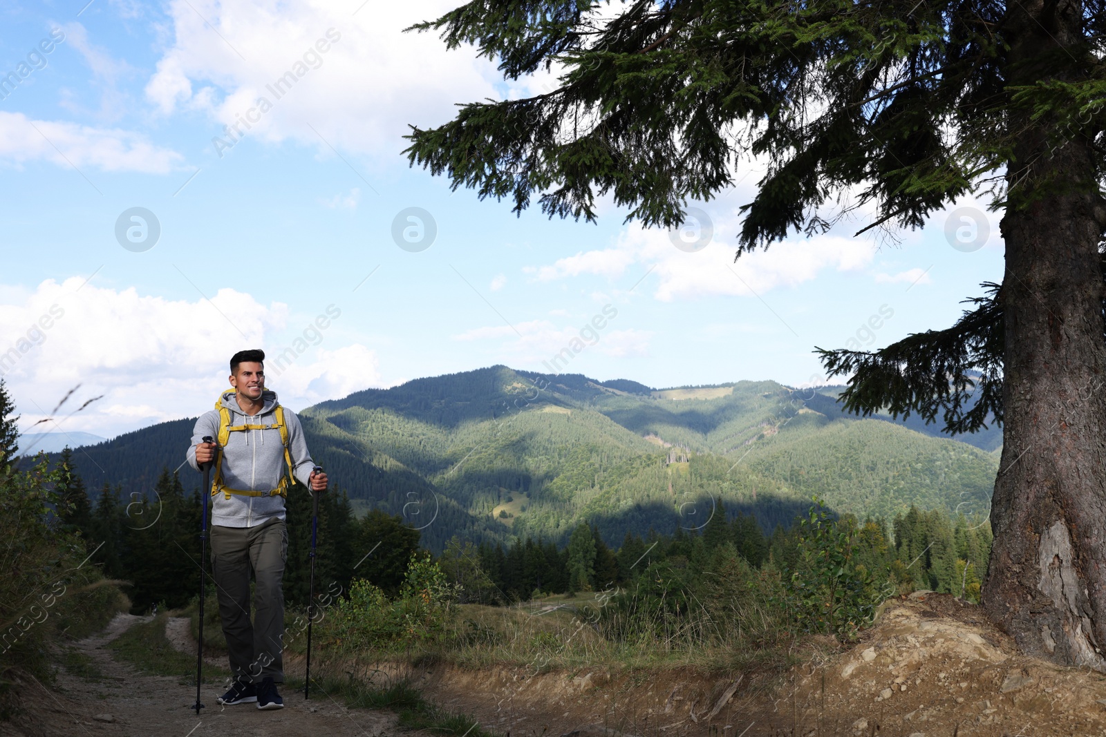 Photo of Tourist with backpack and trekking poles hiking through mountains, space for text