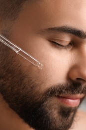 Handsome man applying cosmetic serum onto his face, closeup