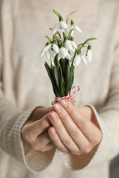 Woman holding beautiful snowdrops with traditional martisor, closeup. Symbol of first spring day