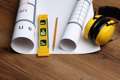 Construction drawings, safety headphones, pencil and bubble level on wooden table