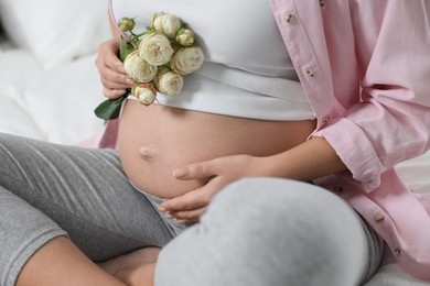 Photo of Pregnant woman in pink shirt with roses on bed, closeup
