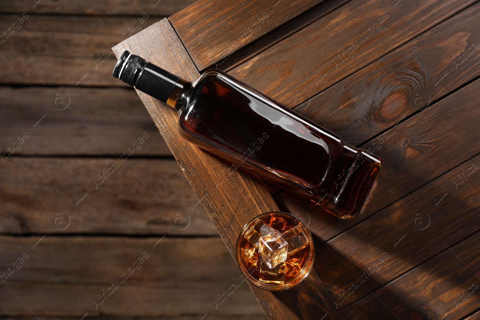 Photo of Whiskey with ice cubes in glass and bottle on wooden crate, top view