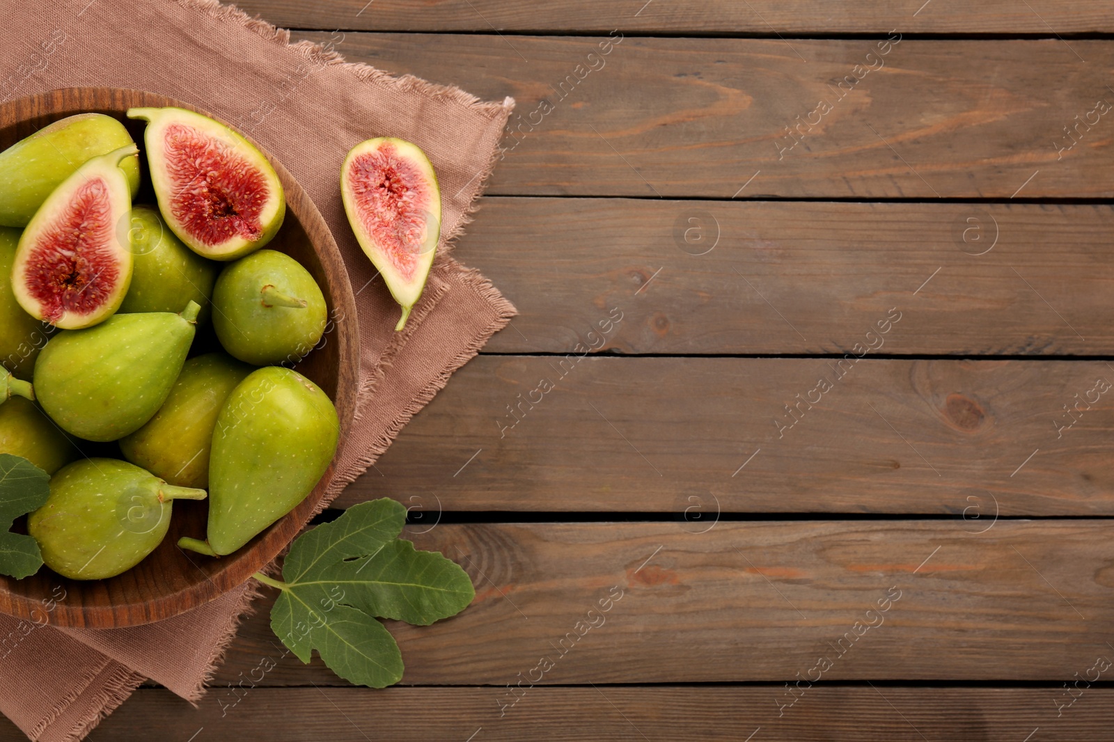 Photo of Cut and whole green figs on wooden table, flat lay. Space for text