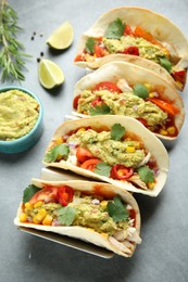 Photo of Delicious tacos with guacamole, meat and vegetables served on grey table