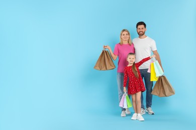 Photo of Happy family with shopping bags on light blue background. Space for text