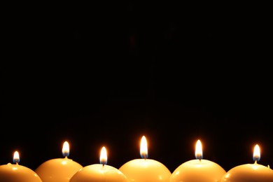 Photo of Many burning wax candles on black background, closeup. Space for text