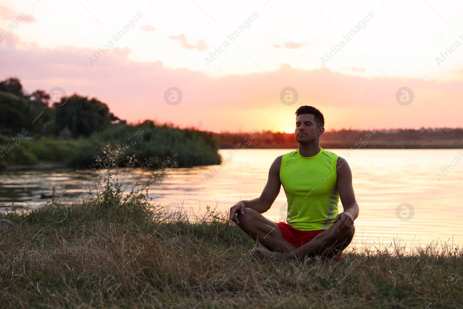 Photo of Man meditating near river in twilight. Space for text