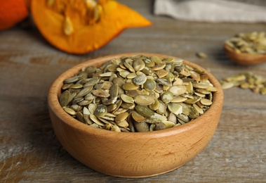 Photo of Bowl of raw peeled pumpkin seeds on wooden table