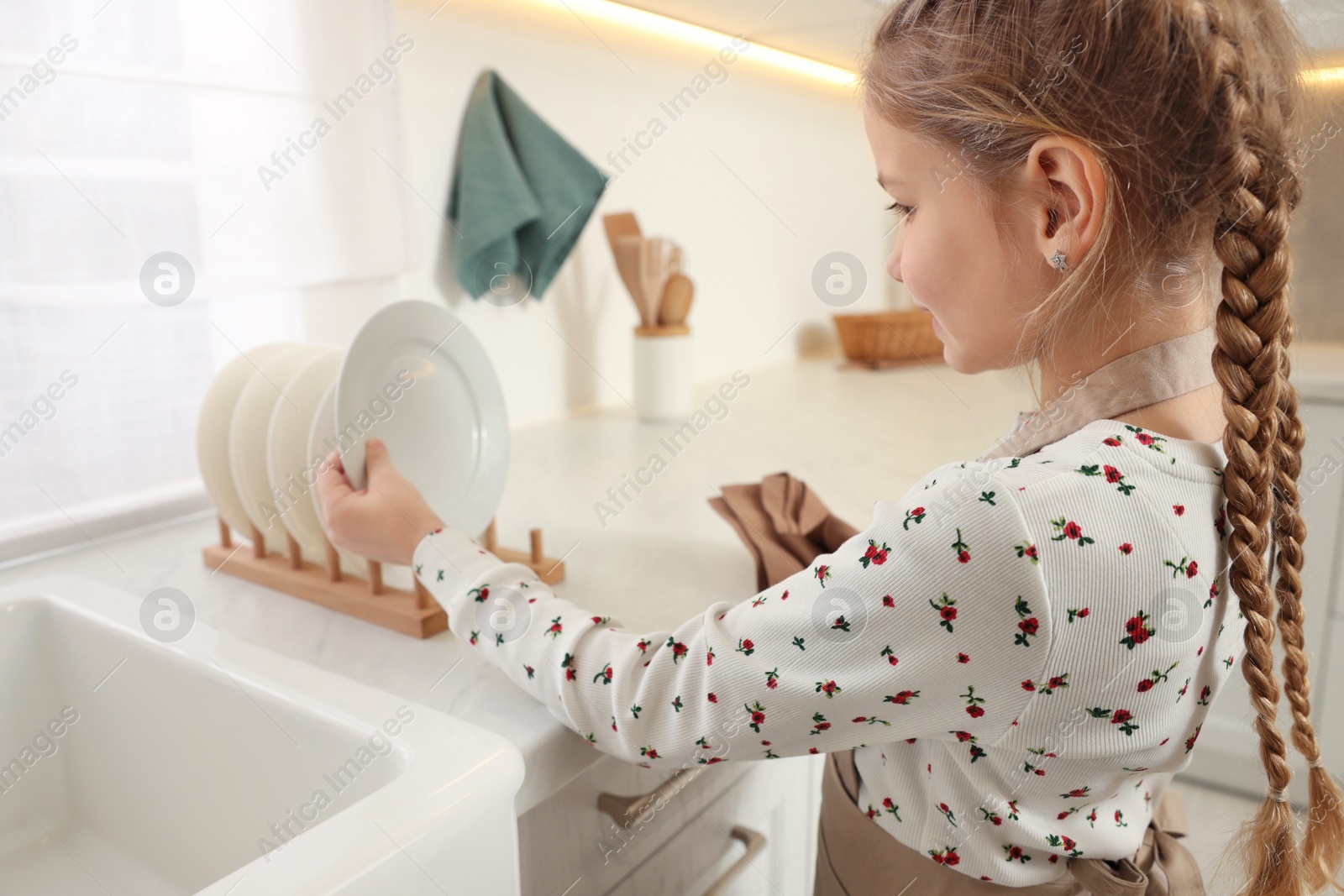 Photo of Girl putting clean plate on drying rack in kitchen