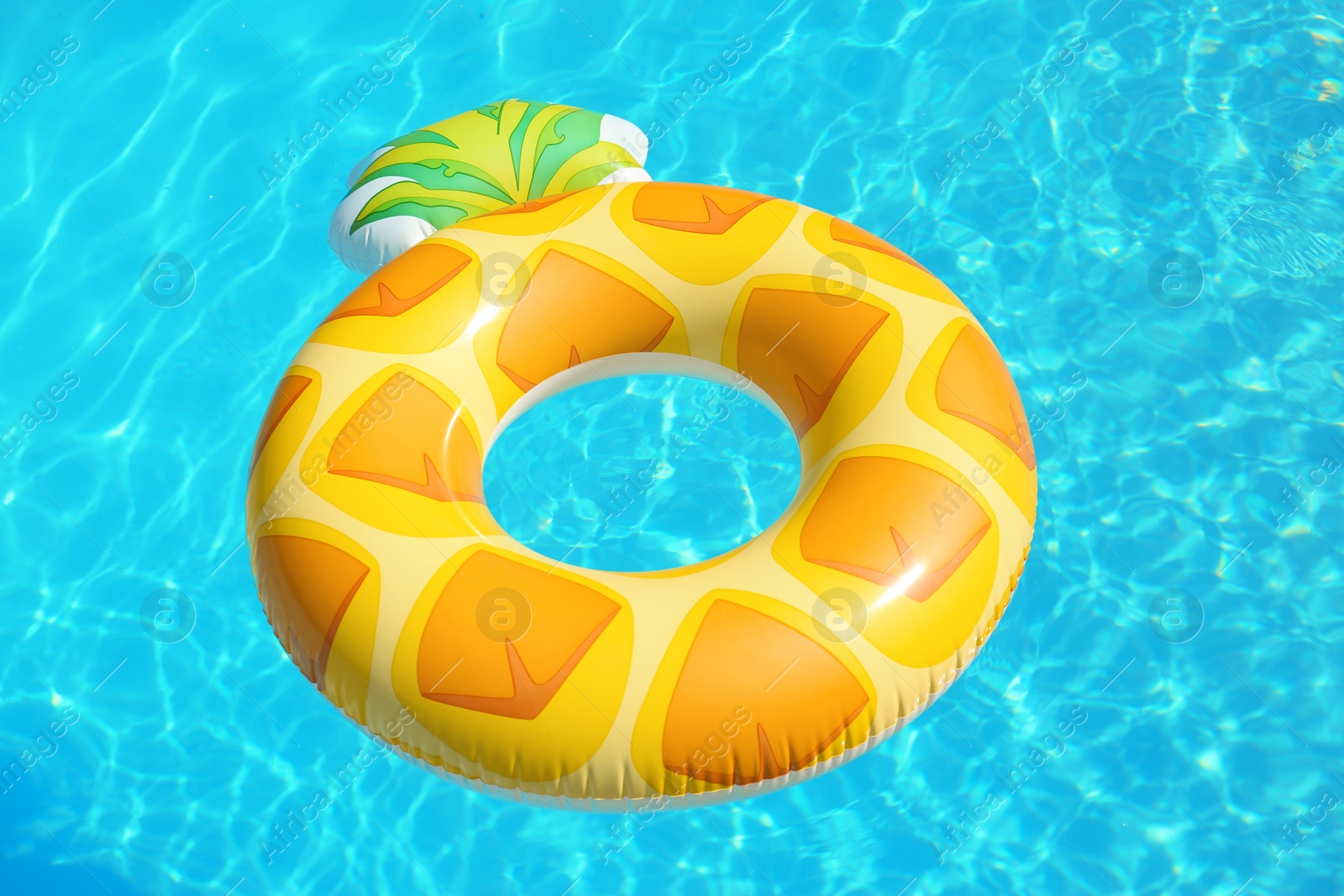 Photo of Bright inflatable pineapple ring floating in swimming pool on sunny day