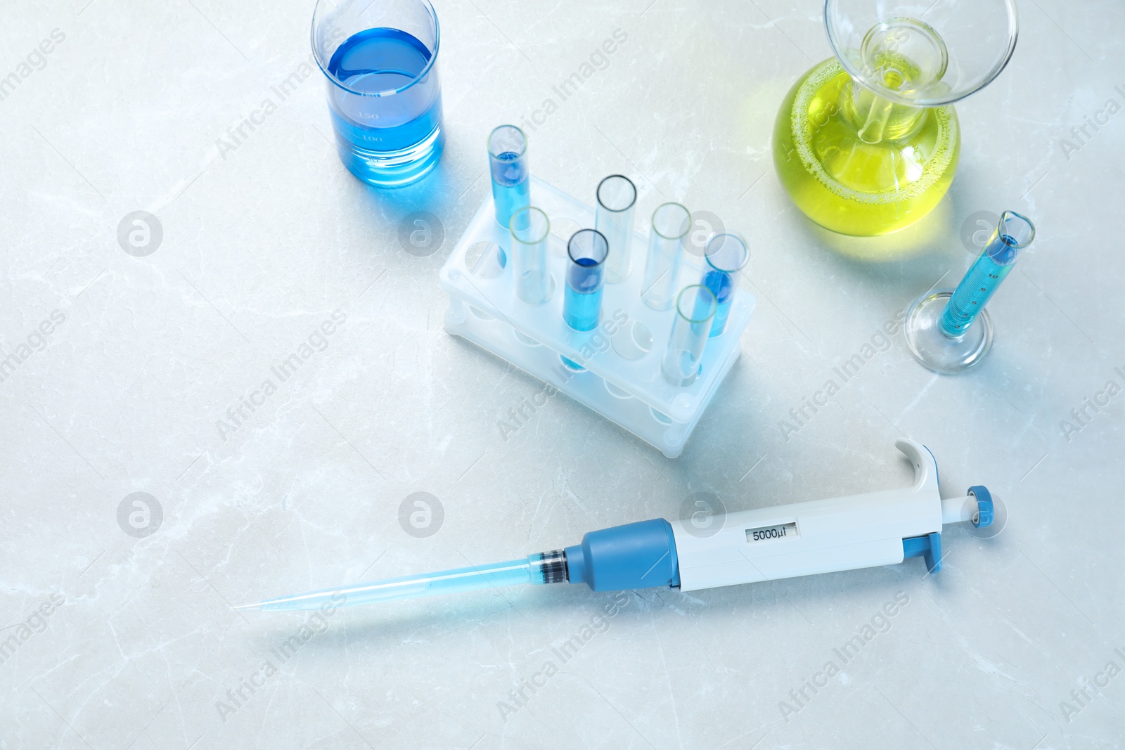 Photo of Laboratory analysis. Micropipette and different glassware with liquids on light grey marble table, above view