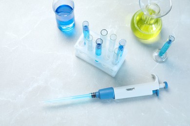 Laboratory analysis. Micropipette and different glassware with liquids on light grey marble table, above view