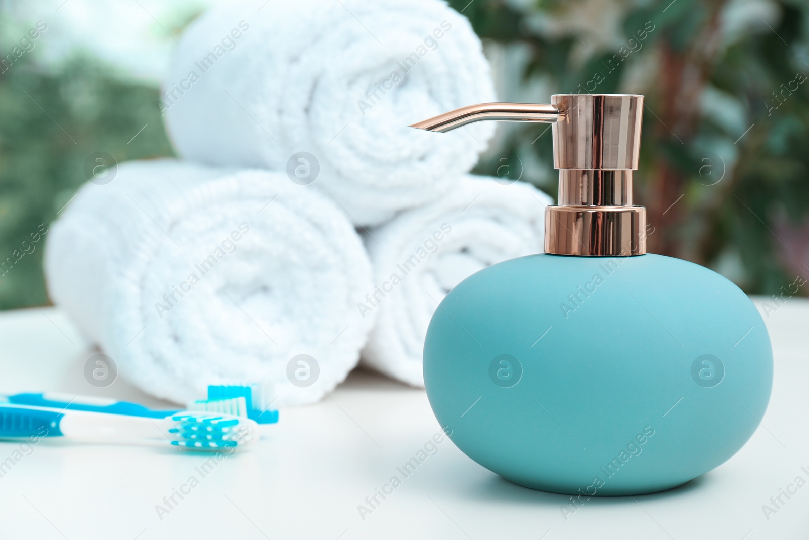 Photo of Soap dispenser and bathroom essentials on table against blurred background
