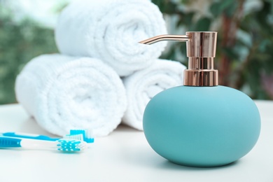 Soap dispenser and bathroom essentials on table against blurred background