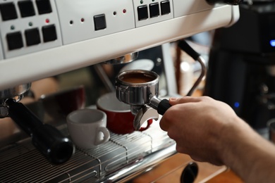 Photo of Barista inserting portafilter into coffee machine indoors, closeup