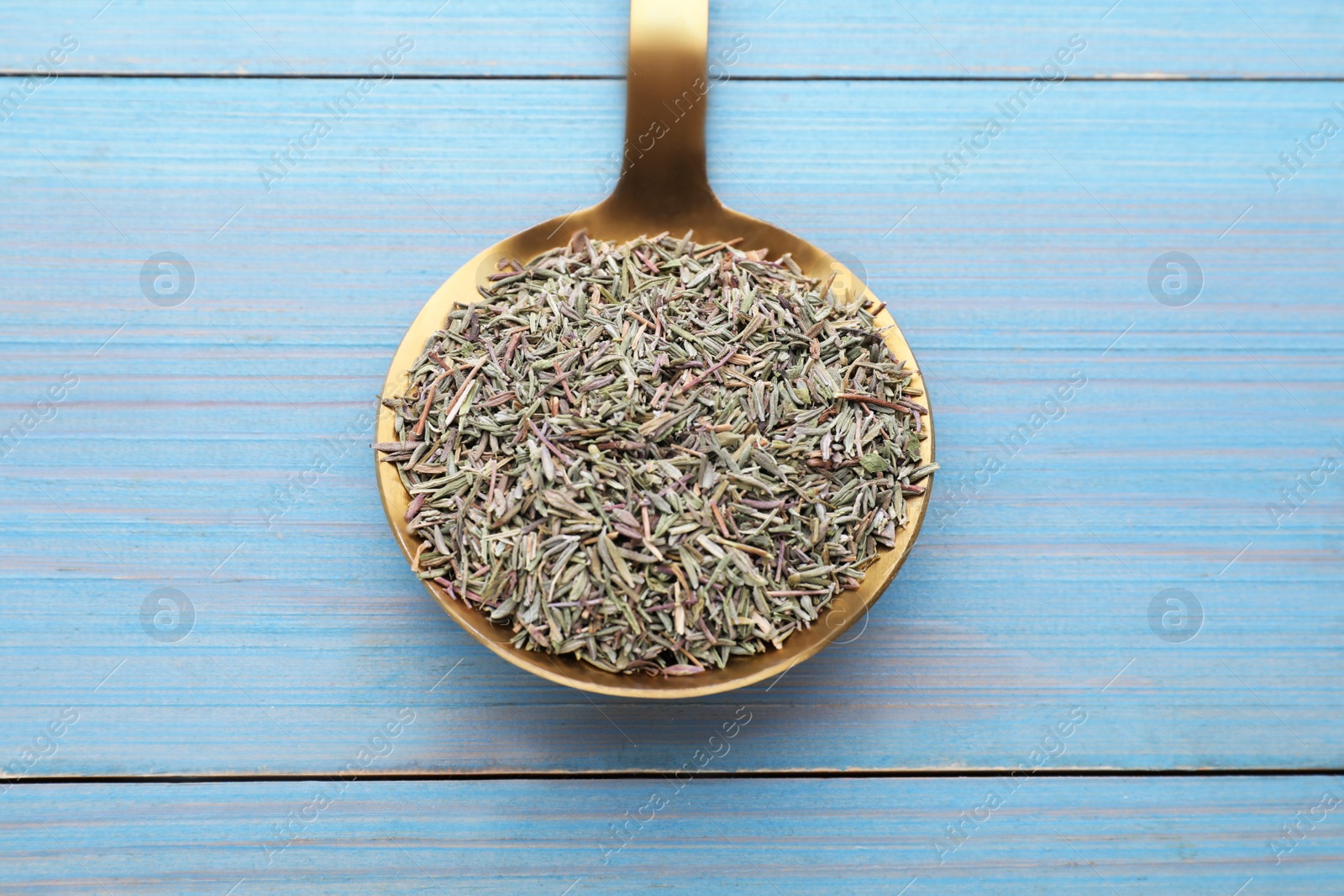 Photo of Metal spoon with dried thyme on light blue wooden table, closeup