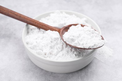 Photo of Spoon and bowl of starch on light gray table, closeup