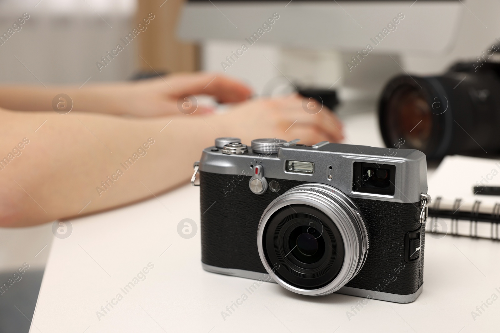 Photo of Photographer working on computer at white table with camera indoors, closeup