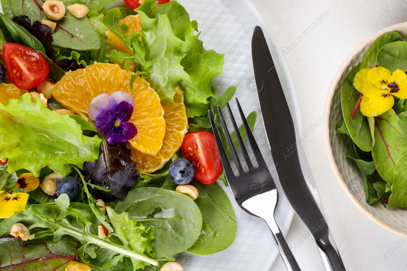 Photo of Delicious salad, ingredients and cutlery on white table, flat lay