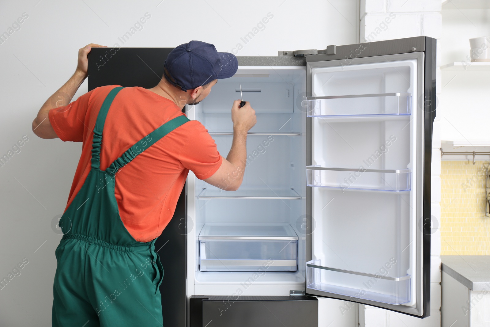 Photo of Male technician with screwdriver repairing refrigerator indoors