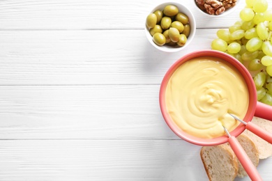 Photo of Flat lay composition with pot of cheese fondue and products on white wooden table, space for text