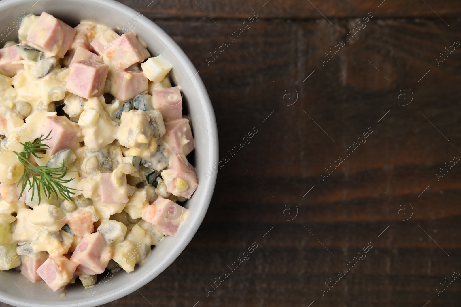 Photo of Tasty Olivier salad with boiled sausage in bowl on wooden table, top view. Space for text