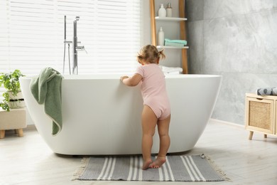 Cute little girl near tub in bathroom, back view