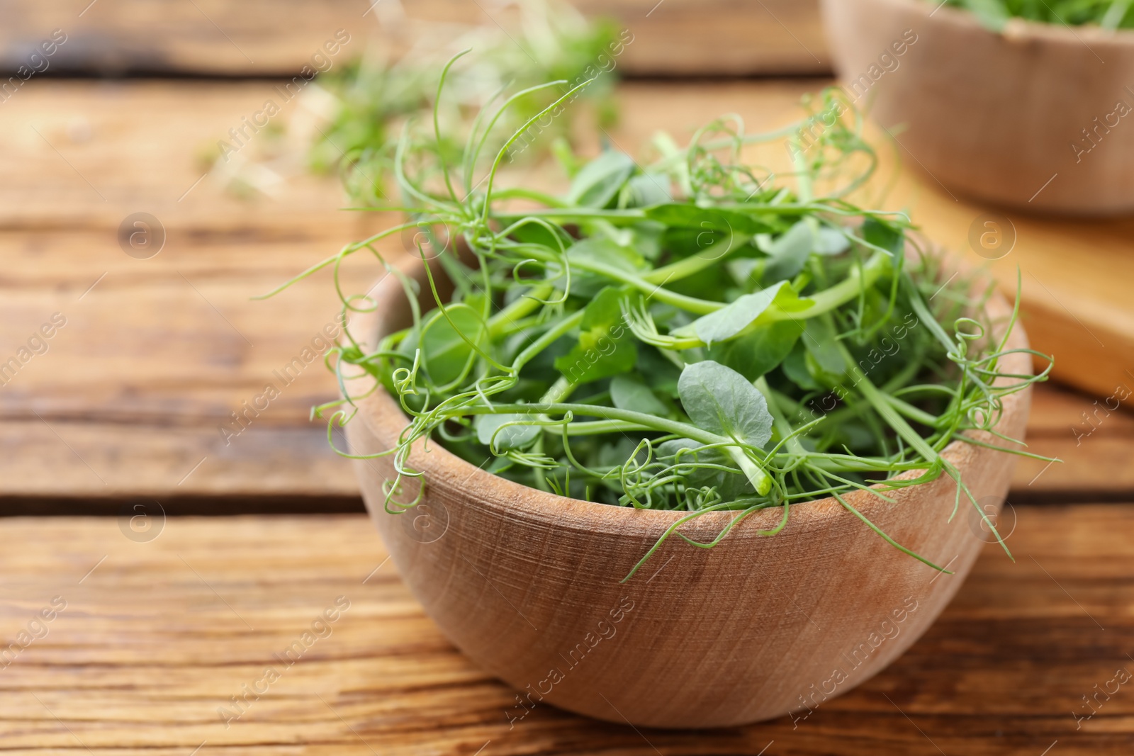 Photo of Bowl with fresh microgreen on wooden table, closeup