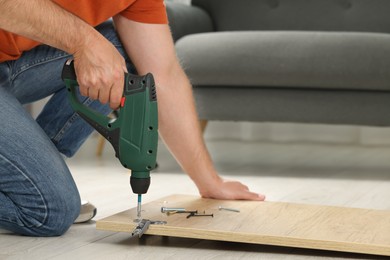Man with electric screwdriver assembling furniture on floor indoors, closeup. Space for text