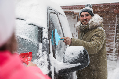 Young couple cleaning snow from car outdoors on winter day