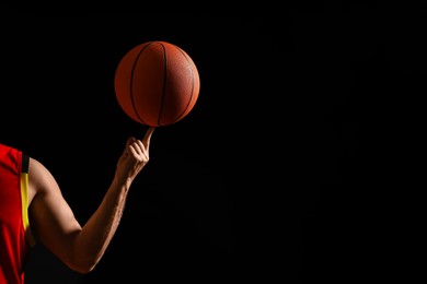 Photo of Basketball player spinning ball on black background, closeup. Space for text