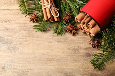 Many cinnamon sticks, anise stars and fir branches on wooden table, flat lay. Space for text