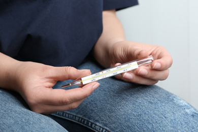 Woman with mercury thermometer on light background, closeup