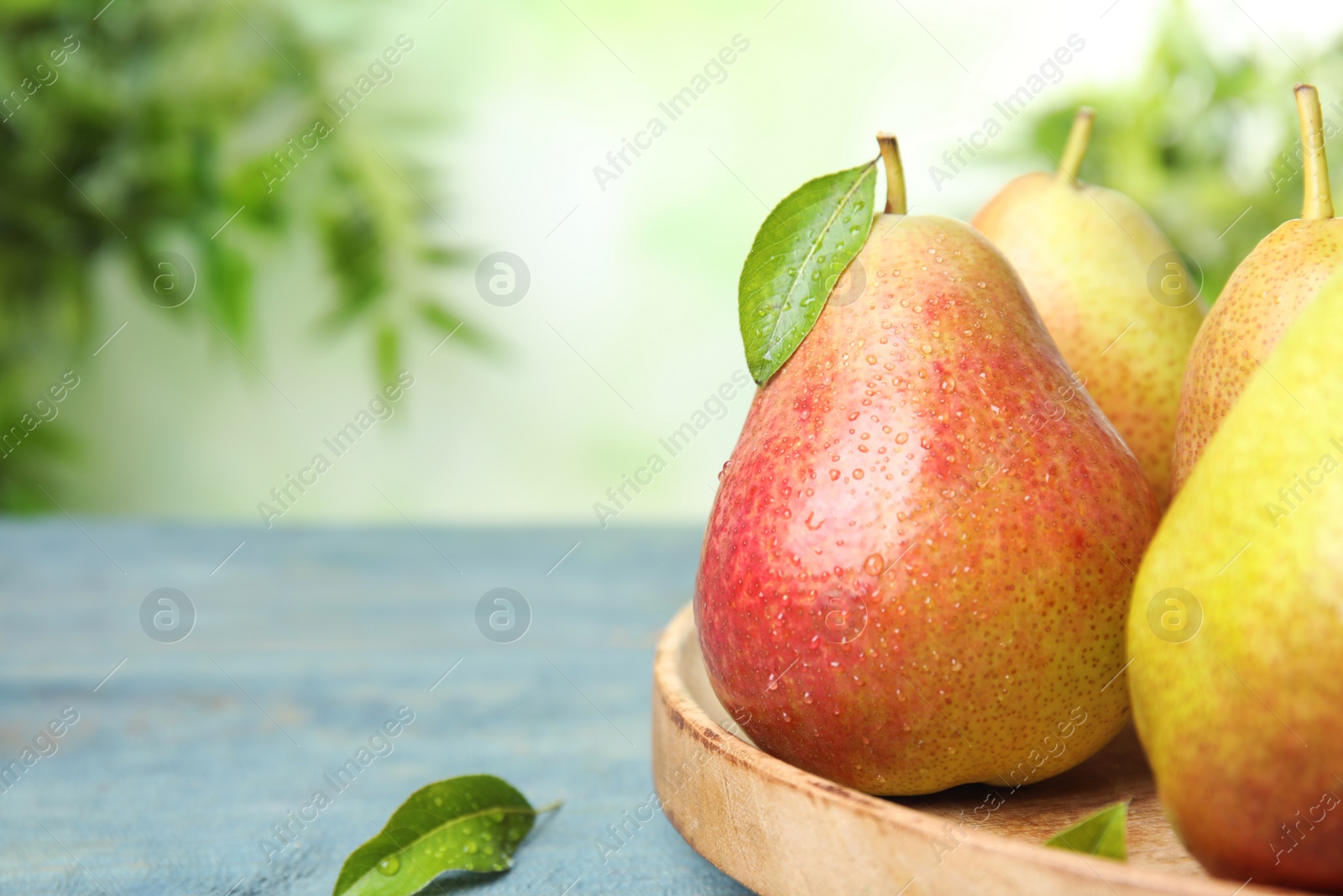 Photo of Ripe juicy pears on blue wooden table against blurred background, closeup. Space for text