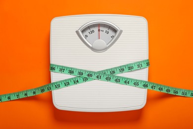 Photo of Bathroom scale tied with measure tape on orange background, top view
